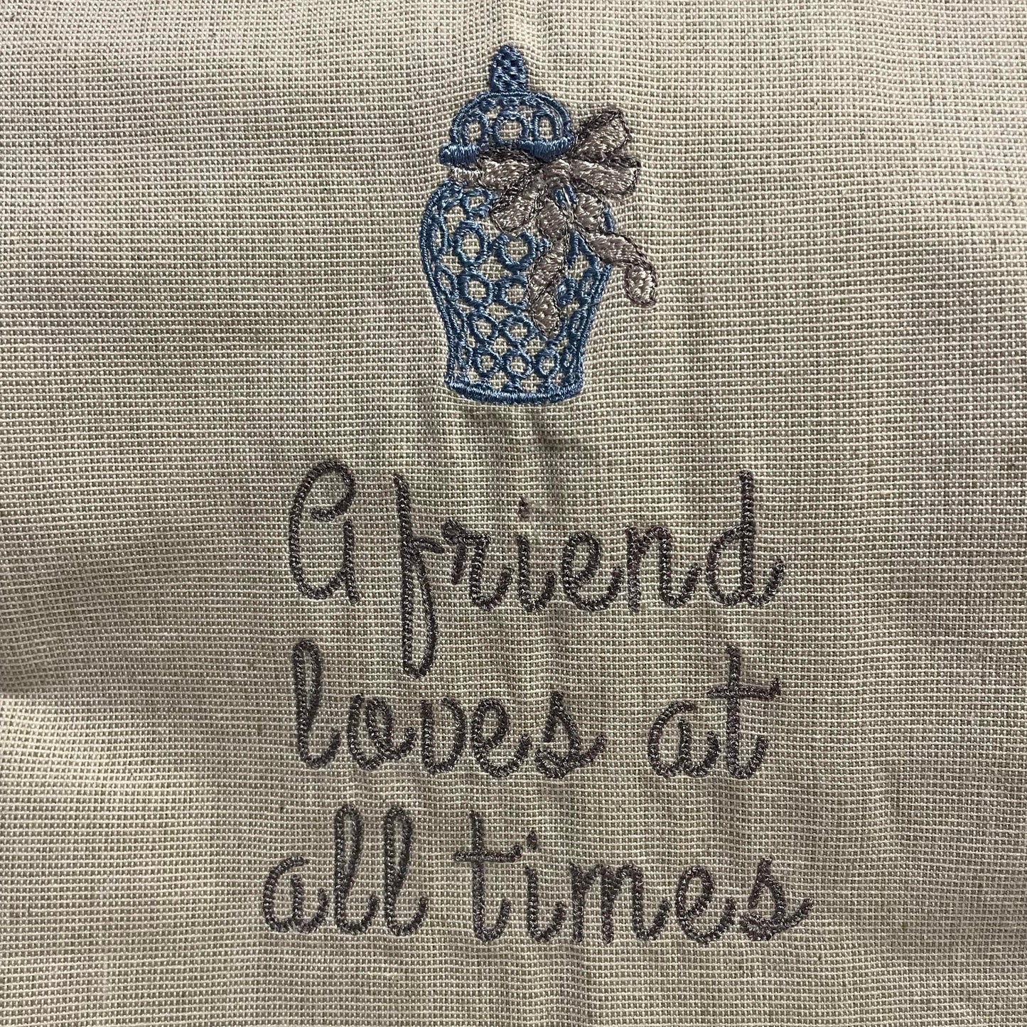 dish towel embroidered with the phrase "a friend loves at all times" and a ginger jar