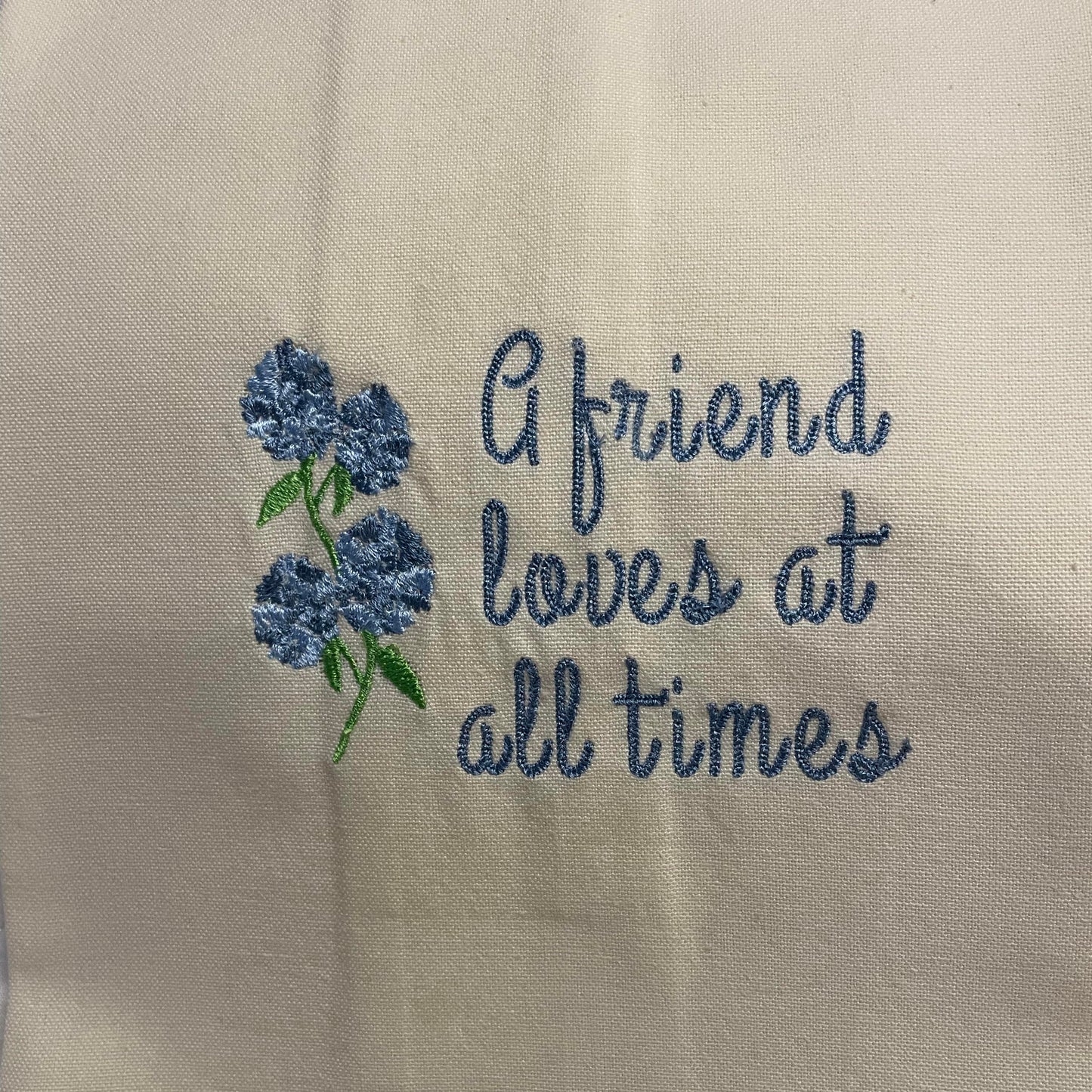 Dish towel embroidered with the phrase "A friend loves at all times" featuring a blue hydrangea